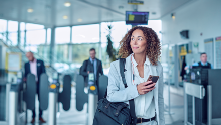 Frau mit Handy in der Hand schaut nach links an einem Flughafen 